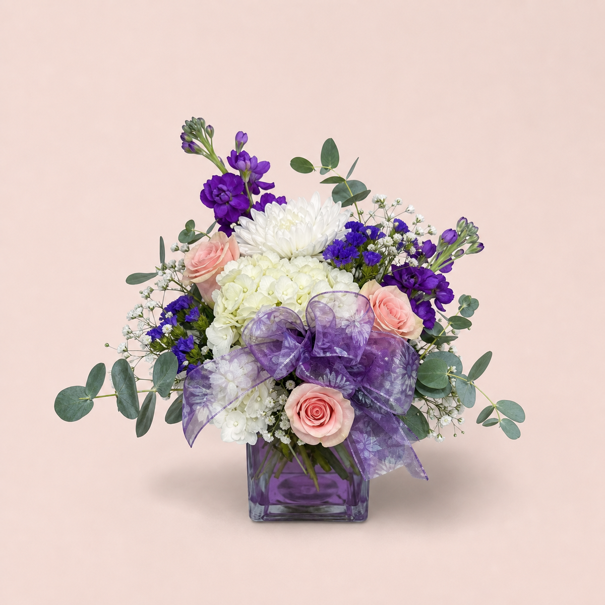 Amethyst Dream Bouquet smaller Standard arrangement with white hydrangea, chrysanthemums, blush roses, purple flowers, eucalyptus, organza bow, and purple cube vase