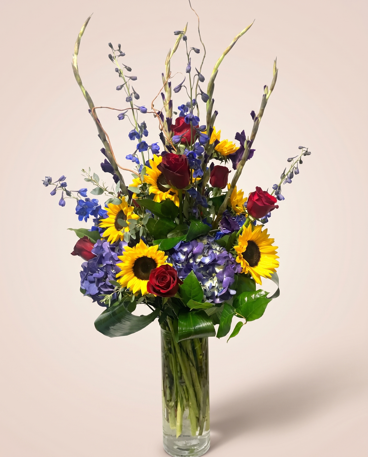 Sunset Meadow Tower — tall sunflowers, red roses, and blue delphinium